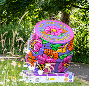 A colourfully decorated beer barrel in a park on a sunny day